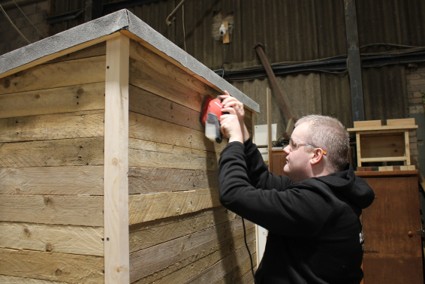 A Trainee sanding a shed with an electric sander
